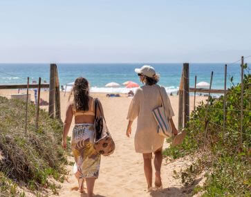 couple walking onto beach with hats and beach bags