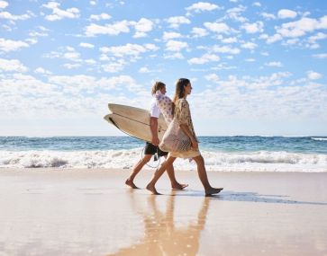 couple striding on sand with surfboards