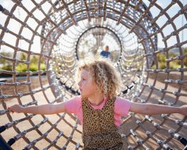 Child climbing through a rope tunnel in a playground surrounded by greenery at Gosford waterfront.