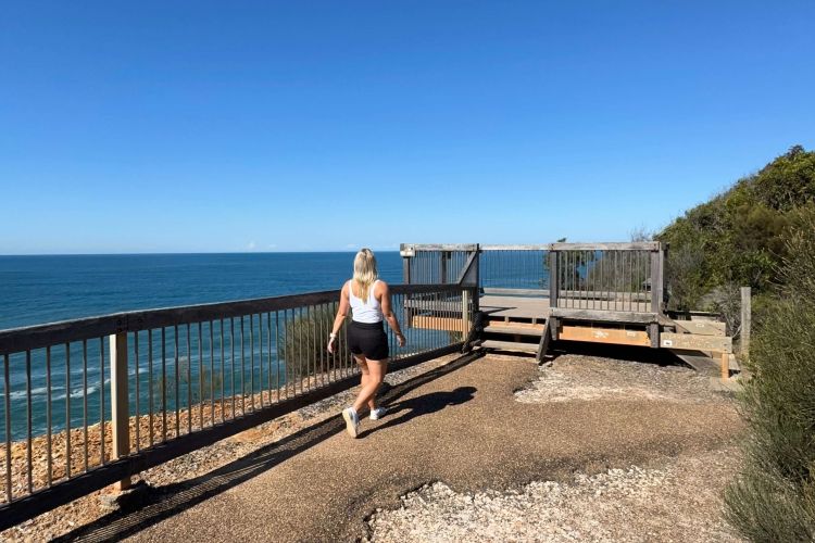 A woman walking towards a viewing platform of the coastline