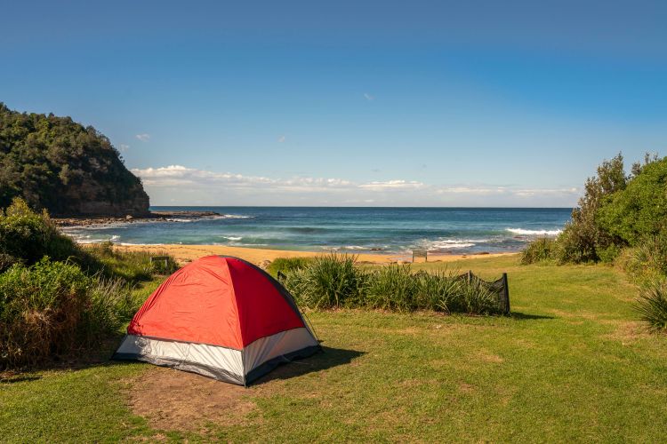 A red tent sits on a grass patch overlooking a beach
