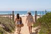 couple walking onto beach with hats and beach bags