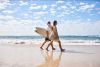 couple striding on sand with surfboards